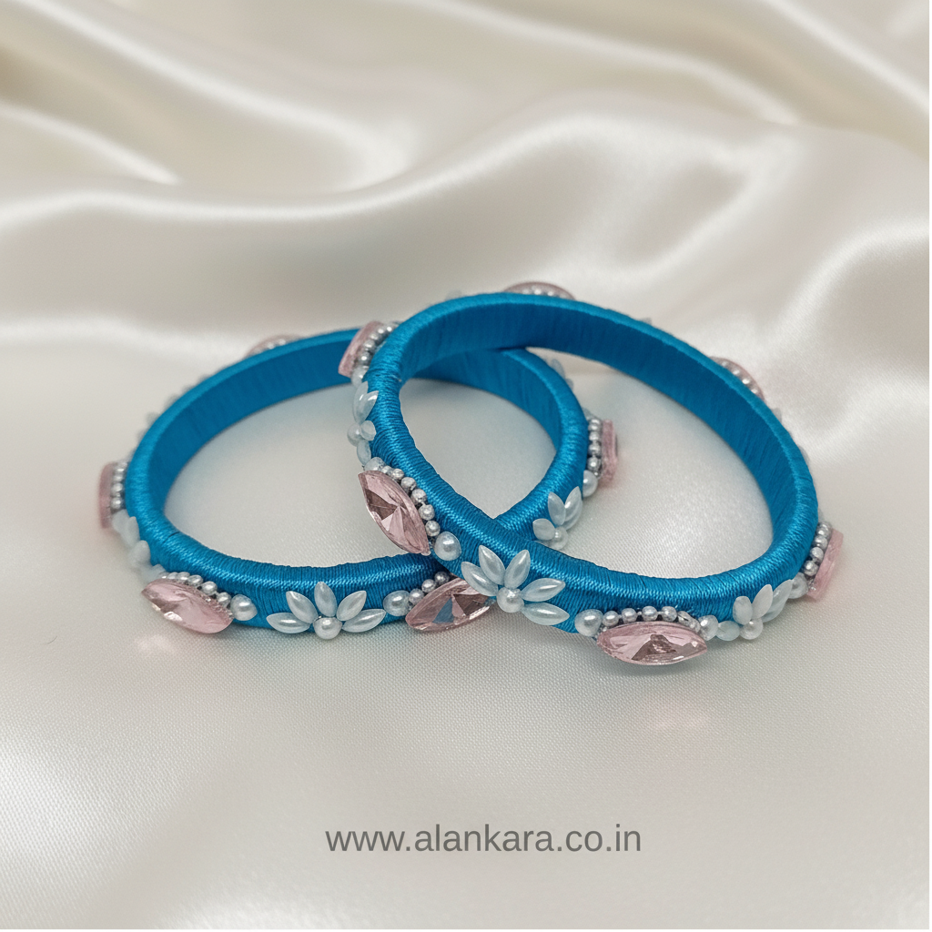 Blue Pearl Crystal Silk Thread Kada Bangles featuring blue silk thread, white pearls, and pink crystals on a satin background.