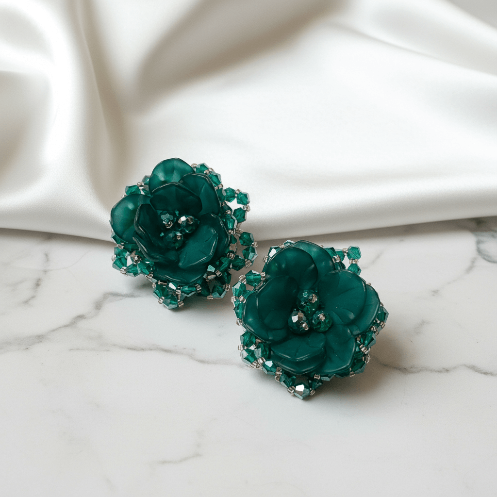 Pair of green floral earrings on a marble surface with a white fabric background