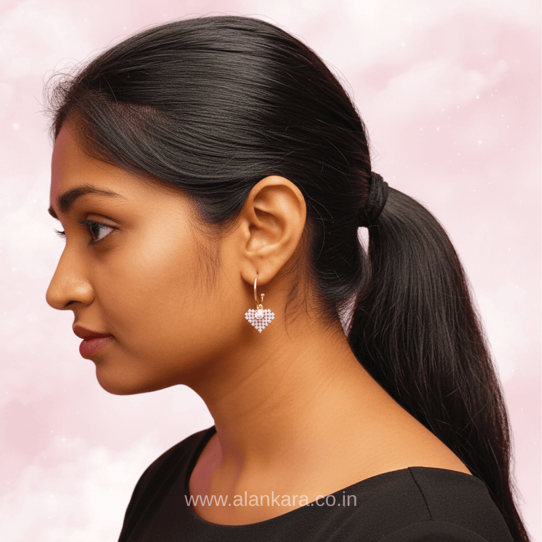 Profile view of a woman wearing Golden Pearl Heart Hoop earrings studded with cubic zirconium against a pink background.