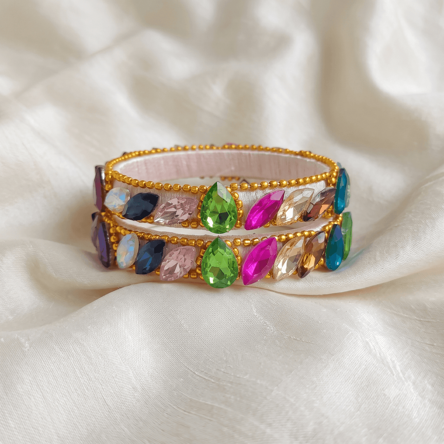 Multicolor White Silk Thread Kada Bangles with colorful crystals and golden bead detailing on a silk background