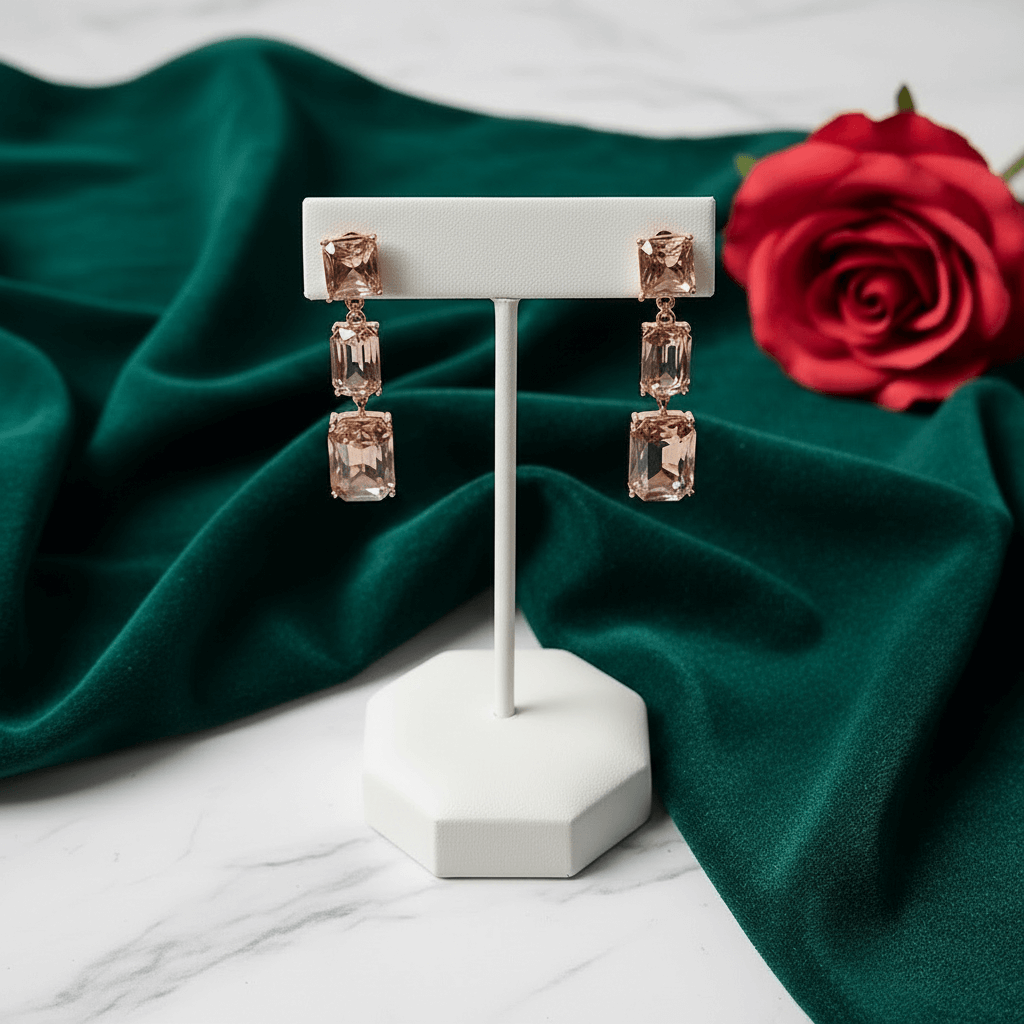 Rose gold earrings on a white stand with a red rose on green fabric