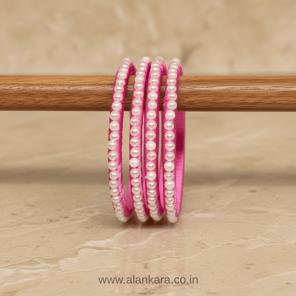 Pink Pearl Silk Thread Bangles displayed on a wooden surface, showcasing their elegant light pink silk and delicate pearl design.