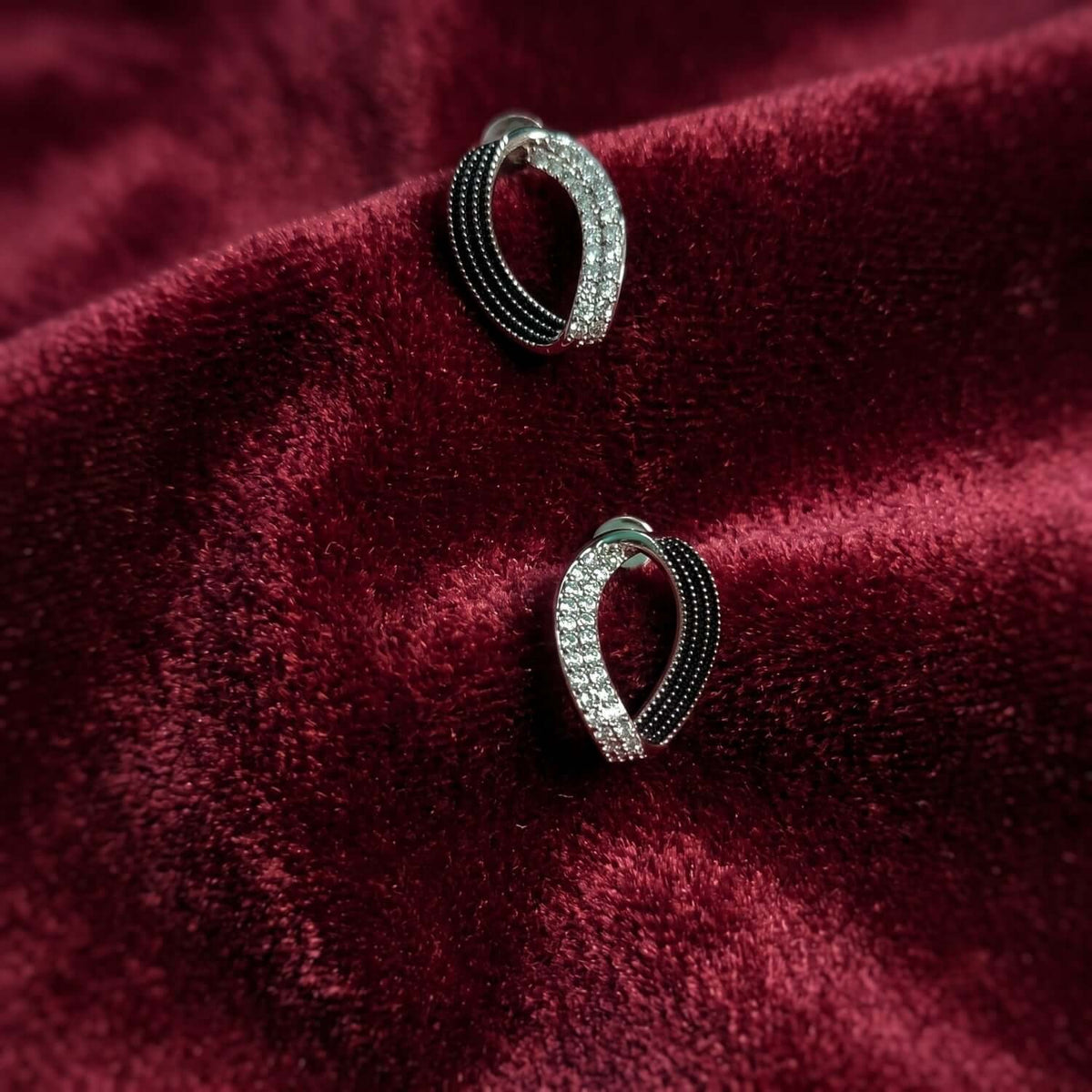 Black White Eye Stud earrings featuring a sleek design with black and white accents on a soft burgundy background.