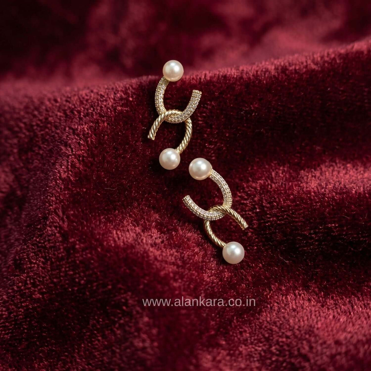 Golden Curve Pearl Stud earring showcasing a gold-plated design with cubic zirconia and pearl details on a rich maroon fabric.