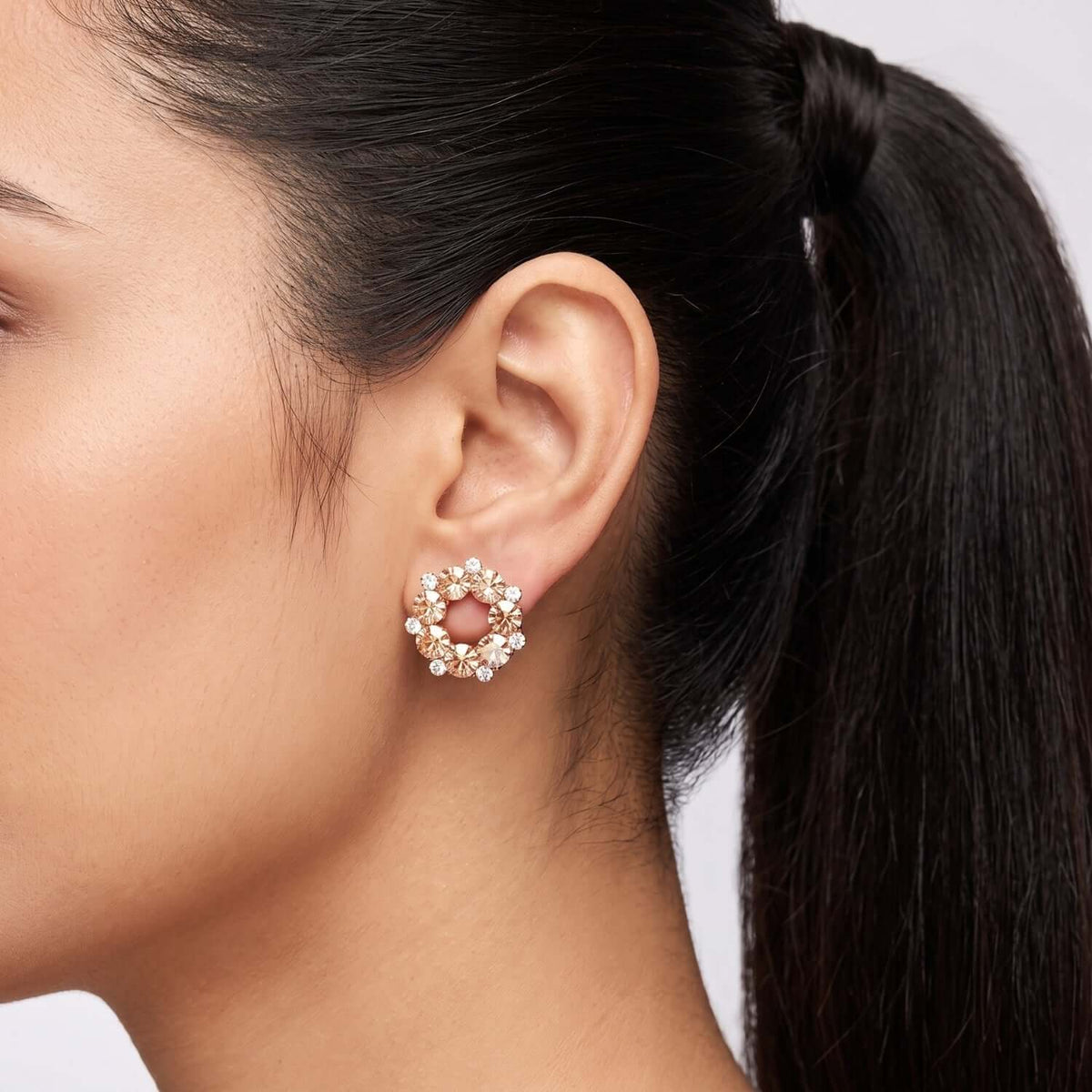 Close-up of a model wearing Peach Crystal Stud earrings, featuring golden alloy and cubic zirconia stones.