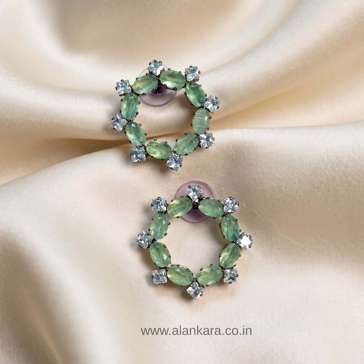 Pista Crystal Stud earrings featuring green cubic zirconia stones on a soft satin background.