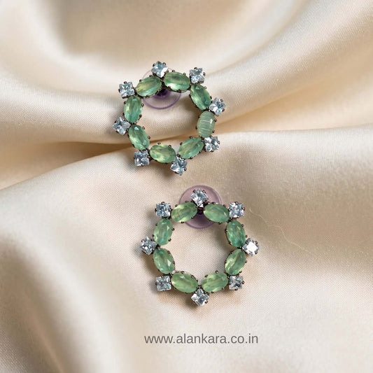 Pista Crystal Stud earrings featuring green cubic zirconia stones on a soft satin background.