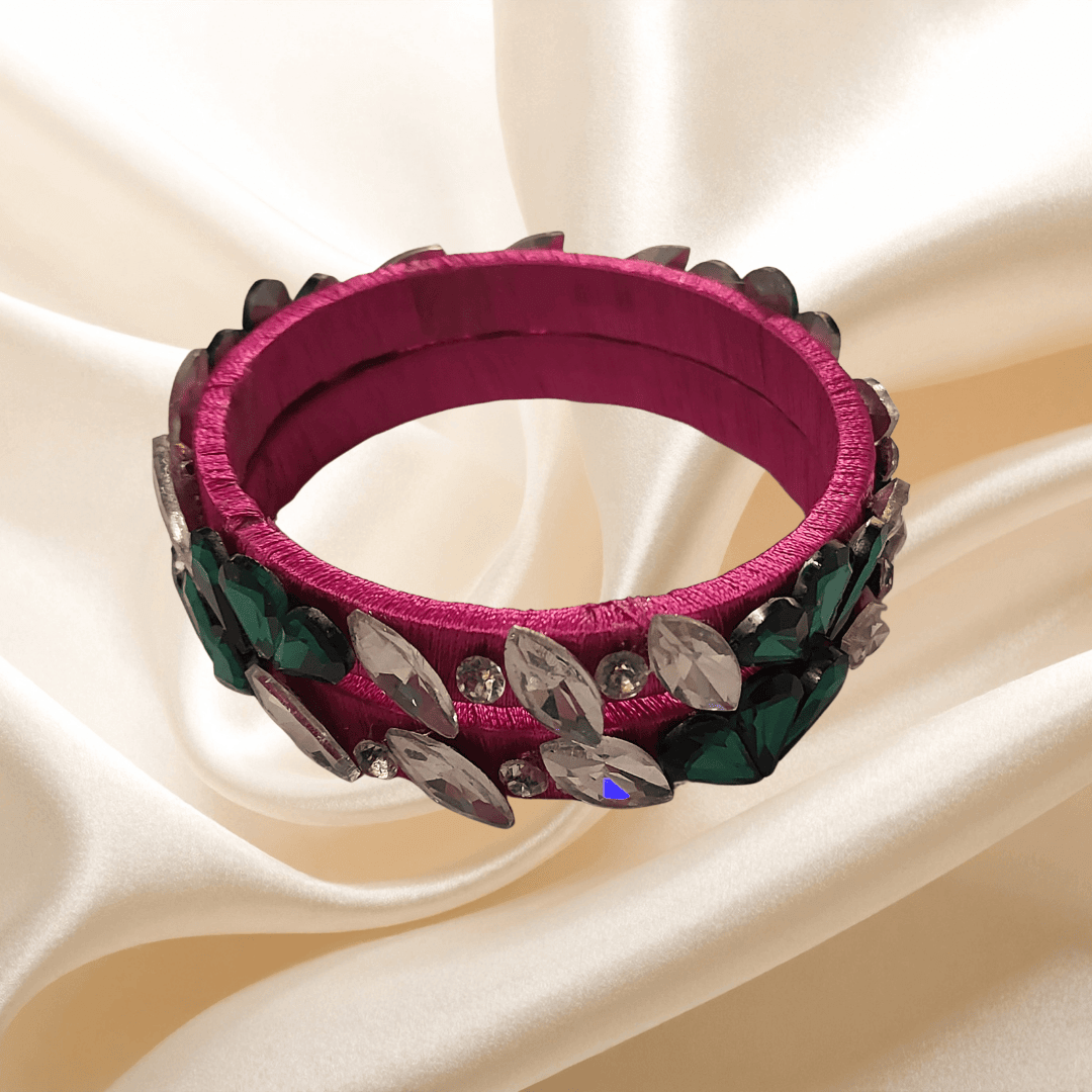 Rani pink floral crystal silk thread bangles with green and clear eye-shaped crystals on a silk background.