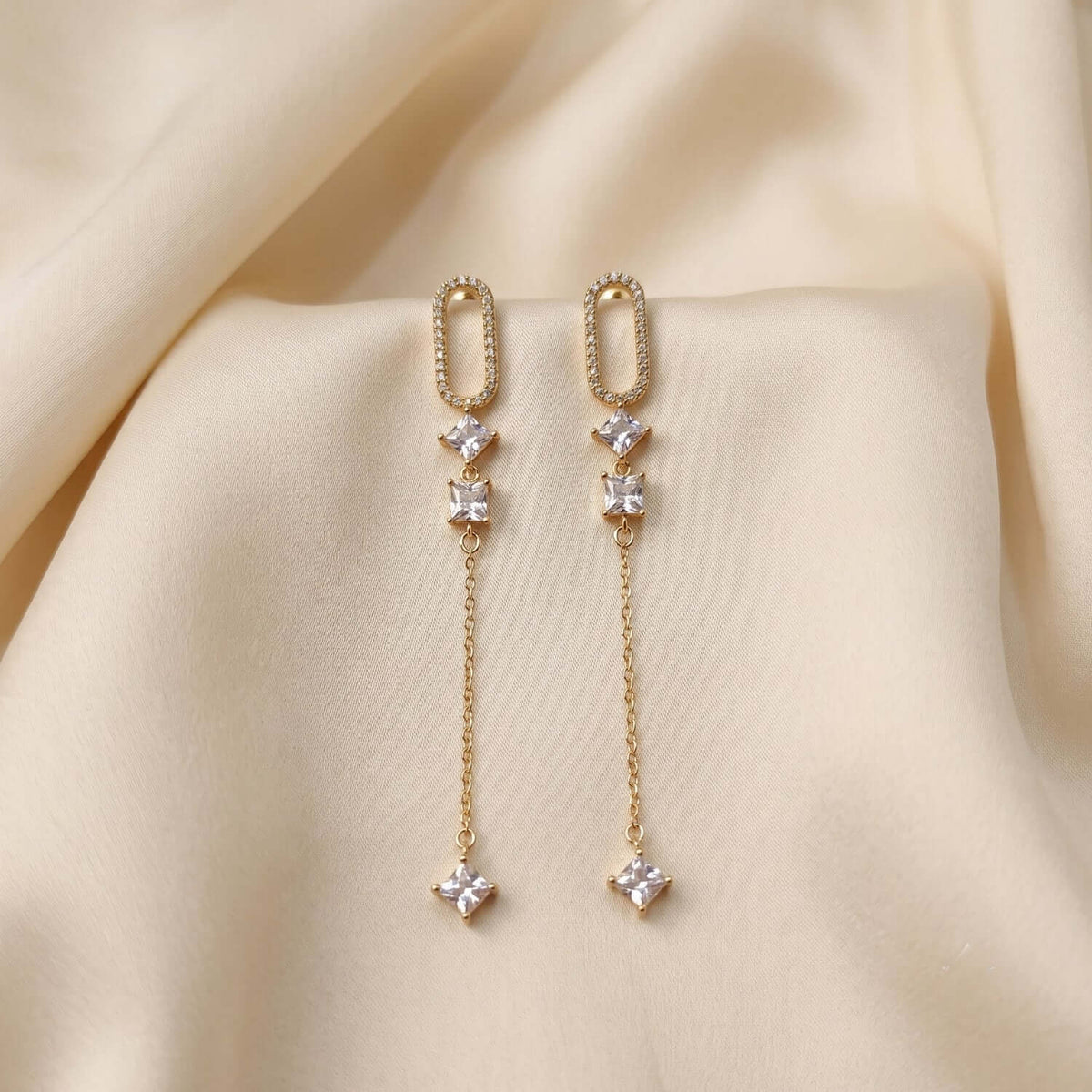 White Capsule Dangler earrings featuring Cubic Zirconia and gold plating on a soft fabric background.
