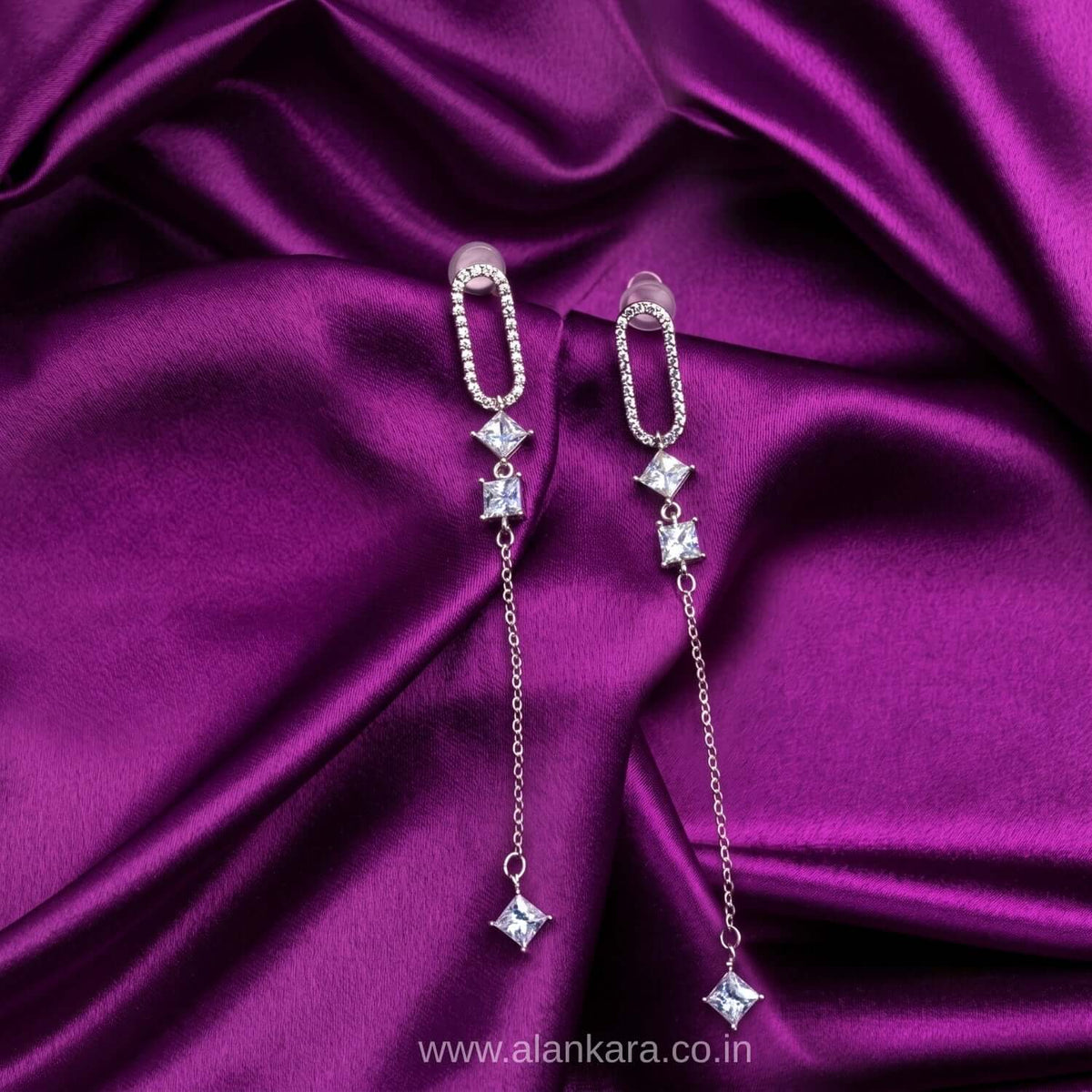 White Capsule Dangler earring featuring cubic zirconia stones on a purple satin background.