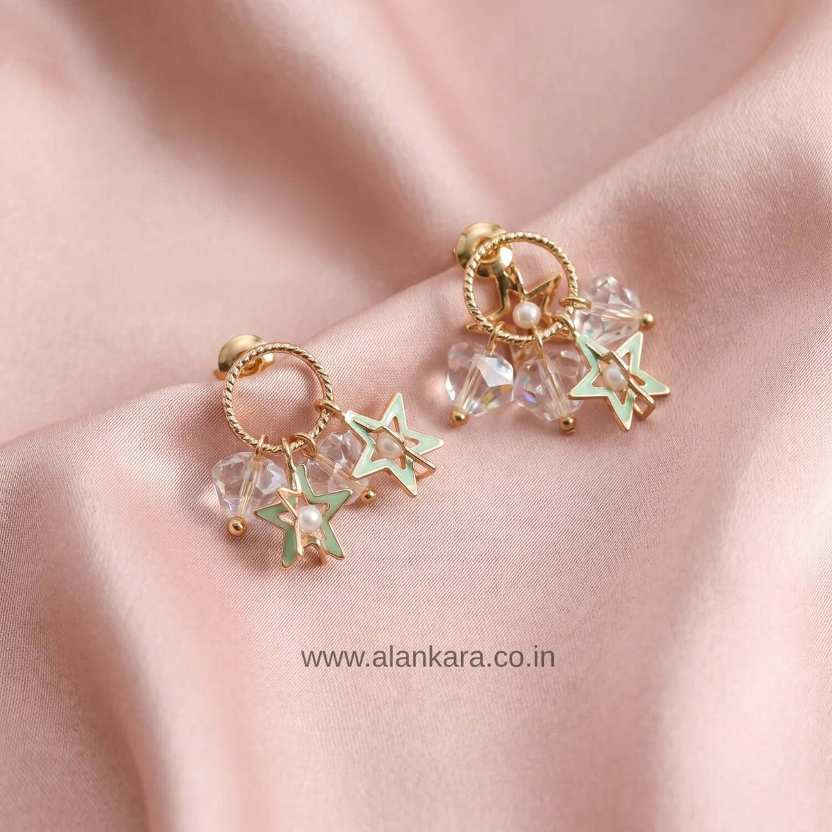 White Crystal Star Stud earrings featuring golden accents and sparkling crystals on a soft pink fabric background.
