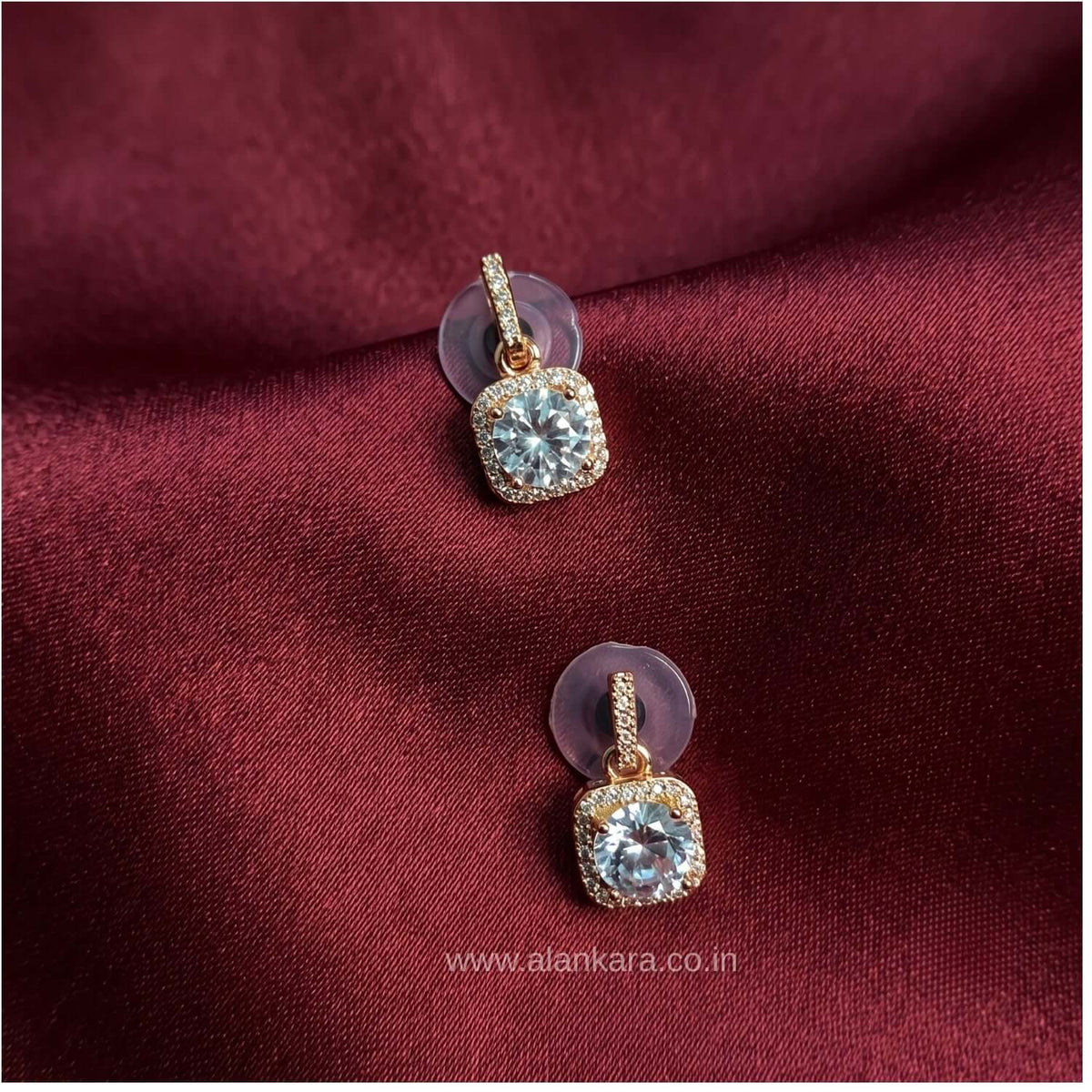 White Rhinestone stud earrings featuring crystal cubic zirconia on rose gold plating, styled on maroon fabric.