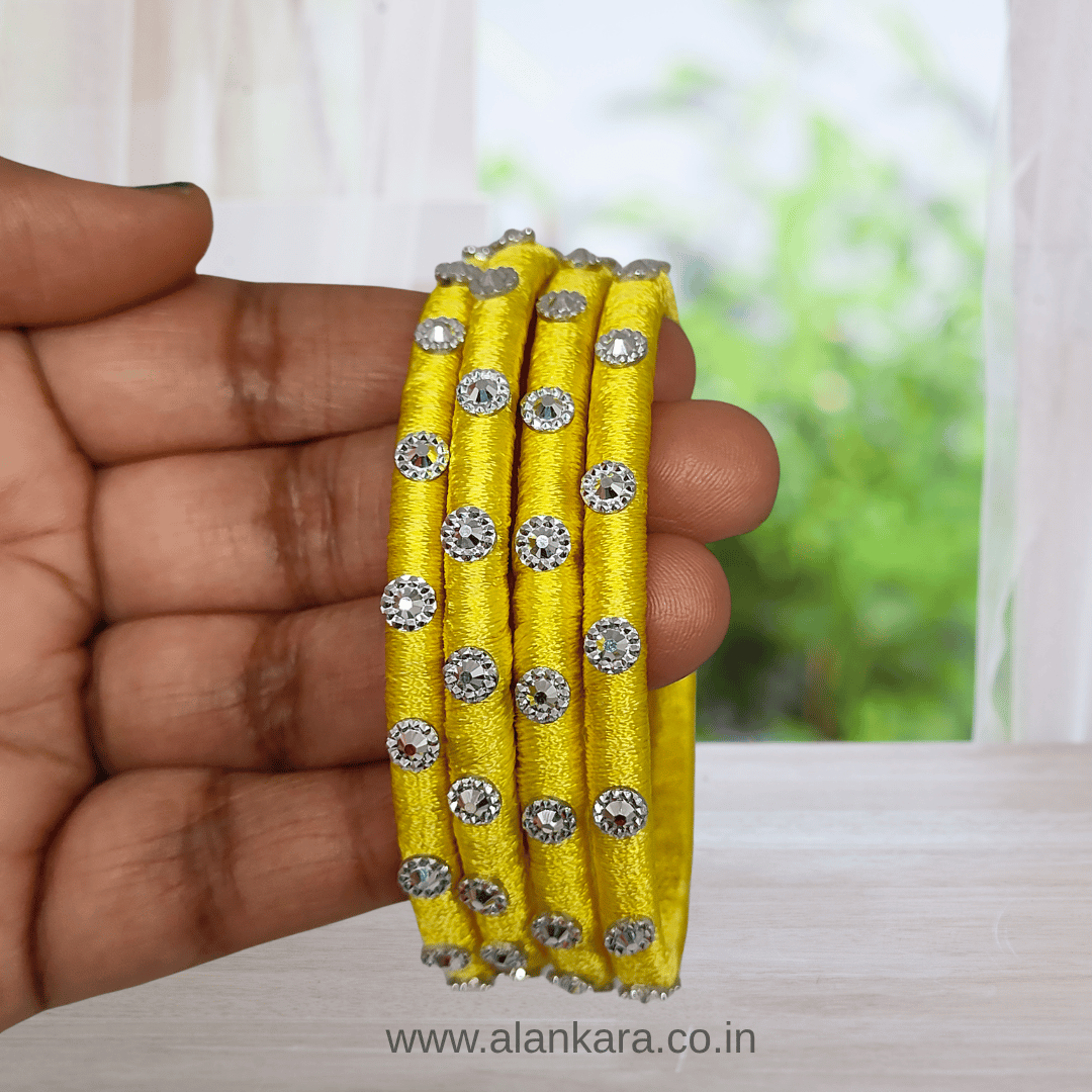 Hand holding Yellow Noori Silk thread bangles embellished with silver Noori work, showcasing vibrant color and style.