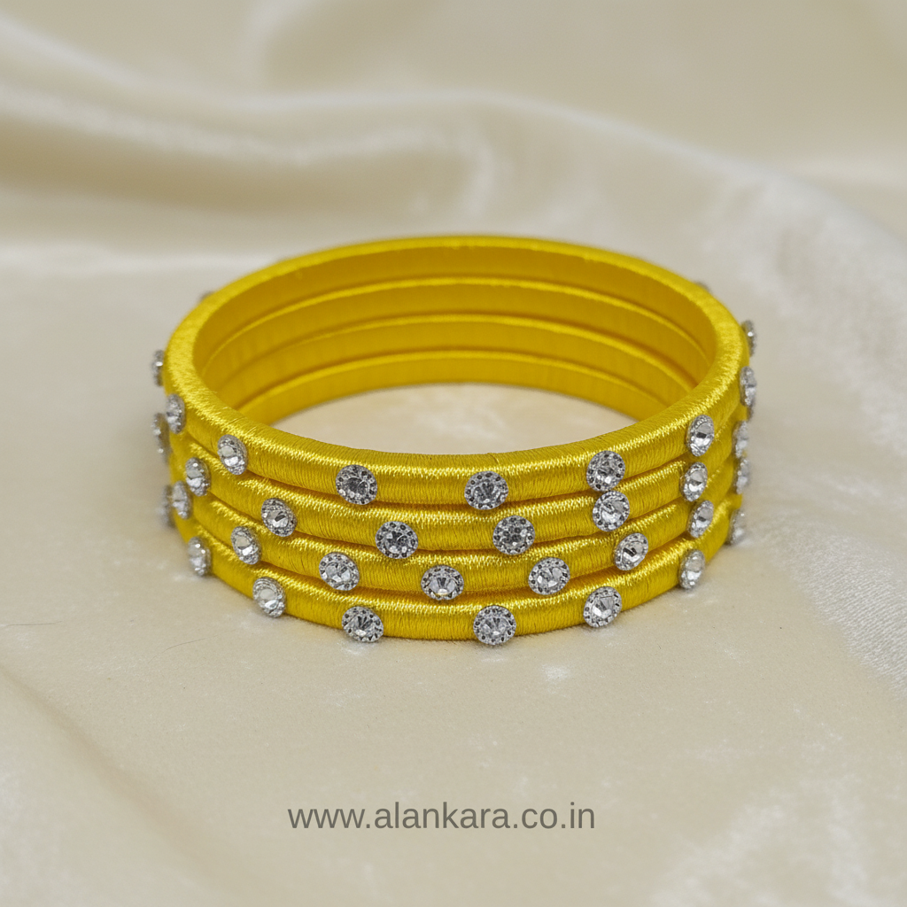 Yellow Noori Silk thread bangles with shimmering silver embellishments on a silk fabric background.