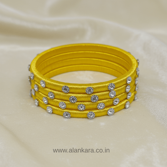 Yellow Noori Silk thread bangles with shimmering silver embellishments on a silk fabric background.